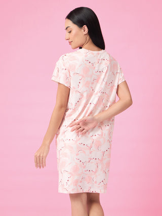 Women's light pink sleep dress with a white and pink cartoon print, viewed from the back, with hands clasped behind her back.