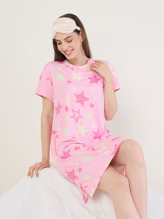 A woman in a pink, star-print nightgown and a pink sleep mask smiles downwards.