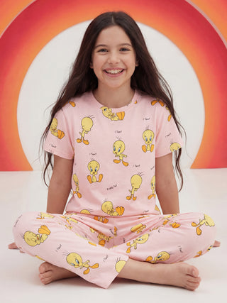 A smiling girl sits cross-legged wearing a pink sleepwear set with an all-over Tweety Bird print.