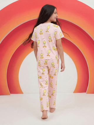A young girl walks away, smiling over her right shoulder, wearing a pink two-piece sleepwear set with an all-over Tweety Bird print.