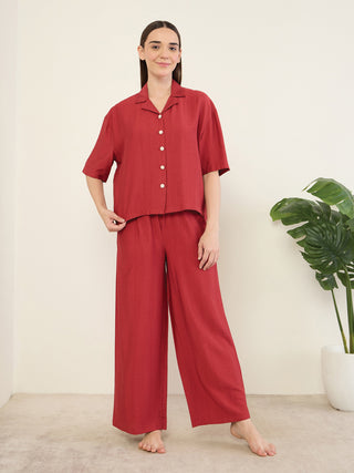Women in a red two-piece pajama set, featuring a short-sleeved collared top with buttons and wide-leg pants, standing with her left hand on her hip.