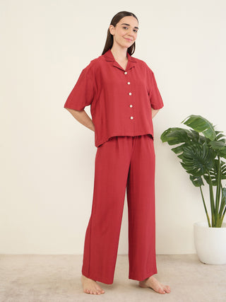 Women in a red pajama set with a short-sleeved top and wide-leg pants, posed against a plain background with a plant.
