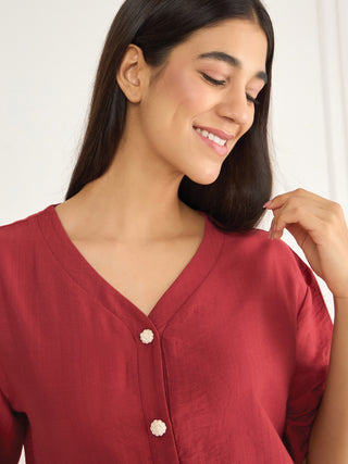 A woman is pictured wearing a maroon V-neck pajama top with two floral buttons.