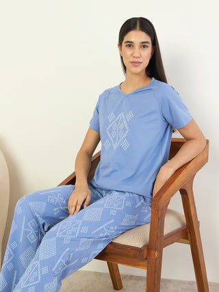 A woman is sitting in a wooden chair wearing blue printed sleepwear.