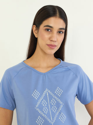 A woman in a blue t-shirt with a geometric print, posing in a studio.