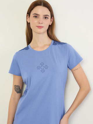Women wearing a blue printed sleep shirt with lace accents on the shoulders and a tattoo of a tree ring on her left arm, posing against a white background.