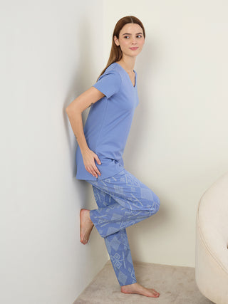Women in a playful pose wear a light blue V-neck t-shirt and matching pants with a geometric print.