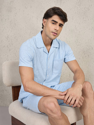 Men in a light blue printed short-sleeve pajama set sitting on a chair.