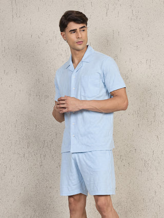 Men wearing a light blue patterned pajama set, with the shirt buttoned up and the man looking to the side.