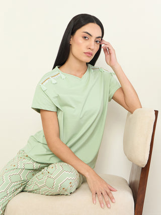 A woman in a light green pajama set with a geometric print, sitting on a chair.