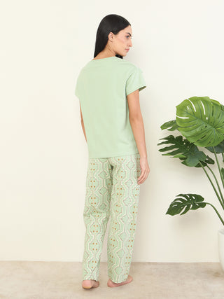 Women's light green printed sleepwear set, posed from the back, standing with a plant.