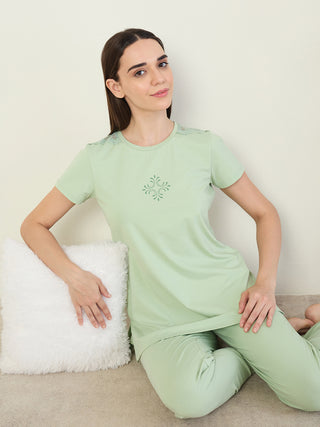 A young woman poses in a light green pajama set, featuring a subtle floral print on the shirt and lace detailing on the shoulders.