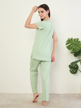 A woman in light green sleepwear, consisting of a t-shirt and pants, is shown from the back, looking over her shoulder.