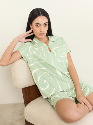 A woman poses elegantly on a chair, wearing a light green printed pajama set.