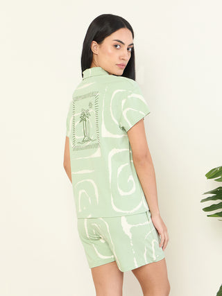 Women in a light green, swirl-printed sleepwear set are posing sideways with their hand in their pocket.