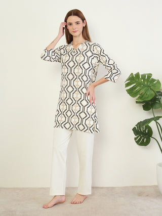 A woman poses in a white tunic with a geometric print and white pants.