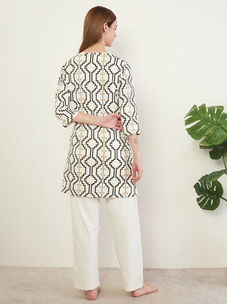 A woman is modeling a white and black geometric print tunic with cream-colored pajama pants.