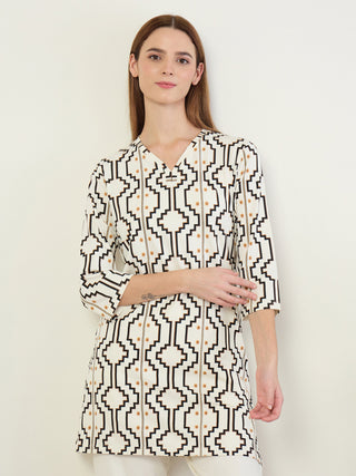 A woman stands in a cream-colored tunic with a black and tan geometric print.