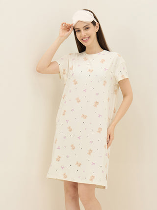 Women in a playful pose wearing a cream-colored short-sleeve nightgown with a teddy bear print and a pink sleep mask.