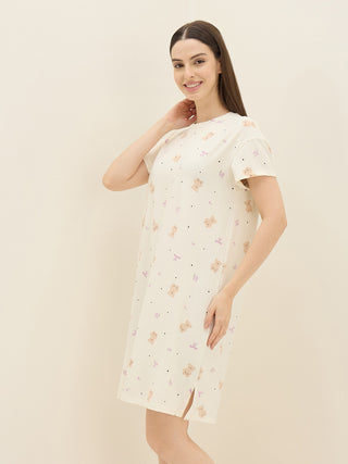 A woman poses in a cream-colored sleepshirt with a playful teddy bear and bow print, featuring side slits for added detail.