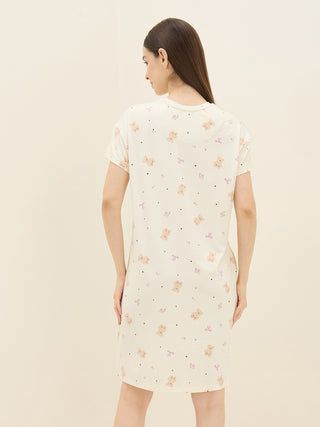 A woman models a cream-colored, short-sleeved sleep dress with a playful teddy bear and bow print.