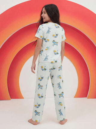 A smiling girl stands with her back to the camera, playfully looking over her shoulder in a light blue two-piece pajama set featuring a repeating print of sleepy Looney Tunes characters.