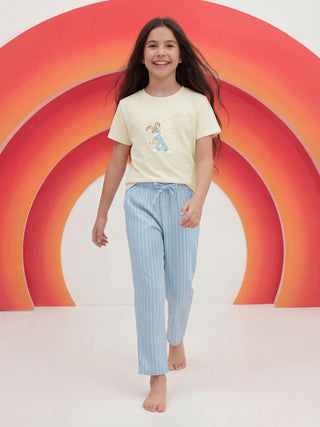 A young girl smiles while walking in a pale yellow t-shirt featuring a cartoon bunny holding a carrot and pink text, paired with light blue pinstriped pajama pants.