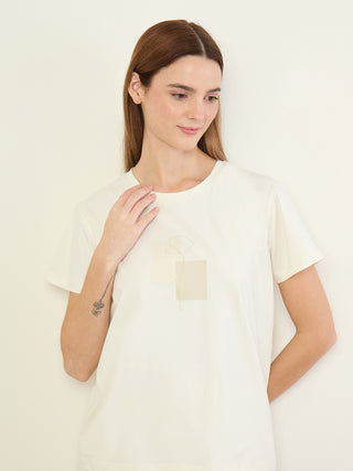 Women in a relaxed pose wearing a cream short-sleeved t-shirt with a subtle floral print and a dot outline.