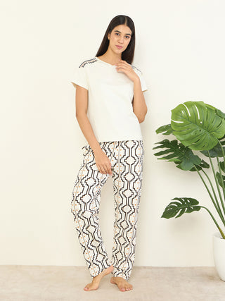 Women wearing a cream-colored t-shirt with embroidered shoulders and matching patterned pants, posing against a plain wall.