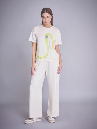 A woman poses in a cream-colored t-shirt with a lime green abstract print and matching cream-colored wide-leg pants.