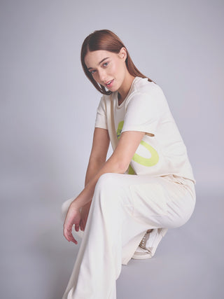 A woman in a cream-colored loungewear set with a lime green graphic print is crouching.