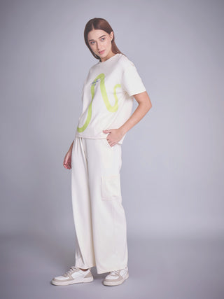A woman models a cream-colored loungewear set with a green wavy print on the t-shirt and wide-leg pants.