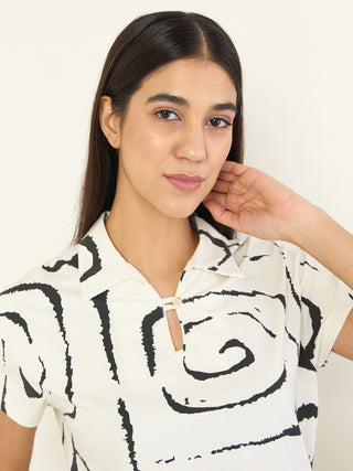 Women in a relaxed pose, wearing a cream-colored pajama set with a black abstract swirl print.