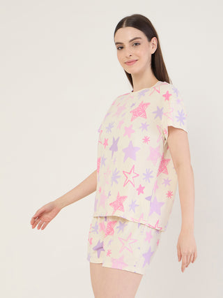 A woman in a pastel yellow pajama set with a scattered star print, featuring a pink outlined star on the top and a purple outlined star on the shorts.