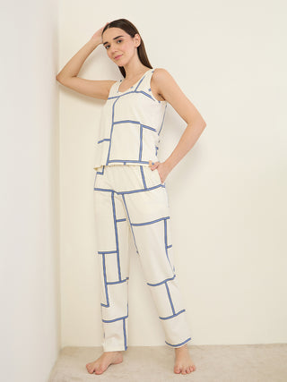 Women in a cream tank top and pants with a blue geometric print, leaning against a wall.