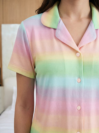 Close-up of a woman wearing a short-sleeved sleepwear top featuring a horizontal pastel rainbow gradient and an open collar.