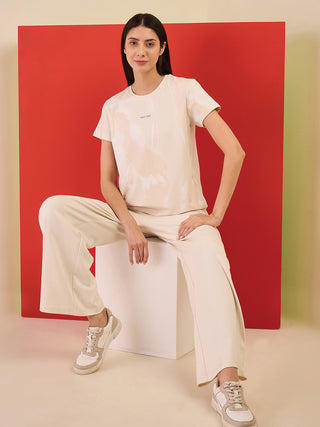 A woman sits cross-legged wearing a cream printed t-shirt and cream wide-leg pants.