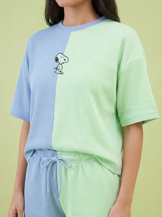 A woman models a bi-color light blue and light green waffle knit sleepwear set, featuring an embroidered Snoopy on the top and matching drawstring shorts.