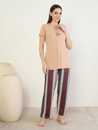 A woman stands posing in a light brown short-sleeved tunic with tassels and decorative trim, paired with patterned sleep pants.
