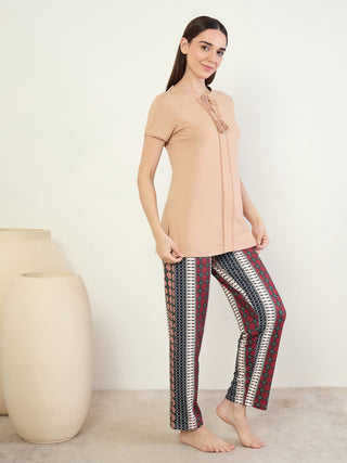 A woman in a beige tunic with tassel trim and patterned pajama pants stands facing left.