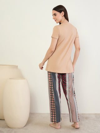 A woman in a beige tunic with tassel trim and patterned pajama pants stands facing left.