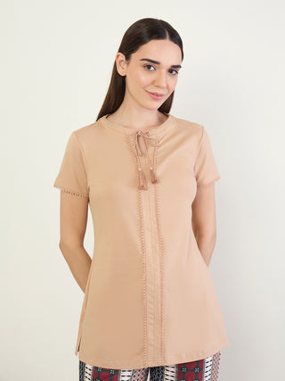 A woman poses in a tan tunic with tassel details and a patterned hem.
