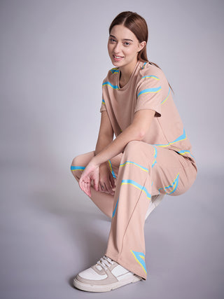 Women in a relaxed pose wear a peach-colored loungewear set with blue and yellow wavy abstract prints.