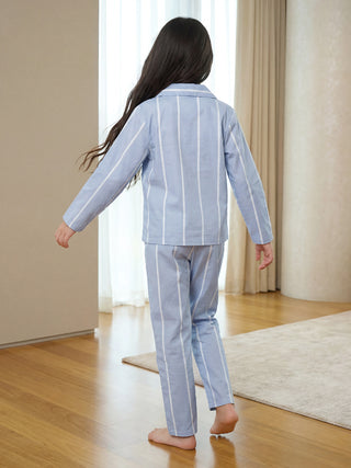 A girl in light blue pajamas with white vertical stripes is seen from behind, walking away on a wooden floor.