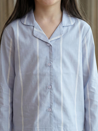 A woman stands wearing a light blue sleepwear top with white vertical stripes and lavender buttons.